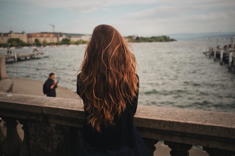 How to Take Care of Wavy Hair. Woman leaning over railing to look at ocean.